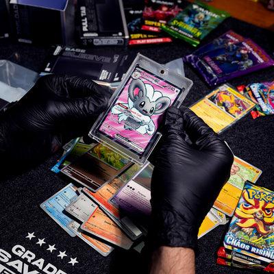 Two hands holding a Pokémon card in a magnetic sleeve. Several booster packs can be seen in the background.