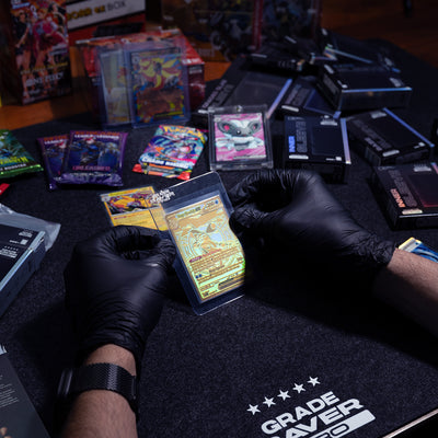 Two hands are holding a Pokémon card in a semi-rigid shield, ready for grading. In the background, you can see a bunch of booster packs and “Grade Saver Pro” products.